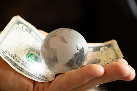 american dollars and a glass globe of the planet lies in the hands of an old woman, finance and peopleの写真素材