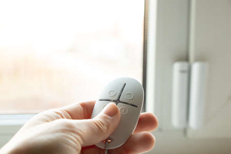 home security system on the windows, an opening sensor and a remote control in the hands of opening and closing, an alarm remote controlの写真素材