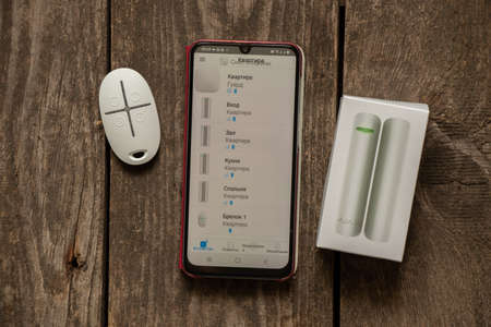 Ukraine Dnipro 11/26/2021 - A new wireless alarm system Ajax lies on a wooden table and a phone with an application, burglar alarm, burglar alarmのeditorial素材
