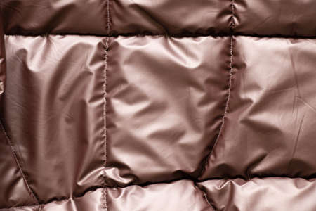 womens quilted bronze brown padded jacket as background, background of soft light fabric of a padded...