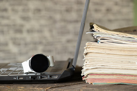 laptop stack of newspapers and smart watch lie on the desk at home, laptop and magazines on the tableの写真素材