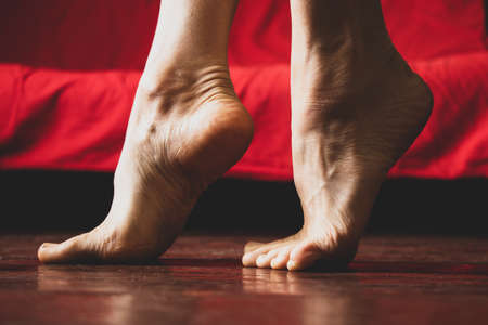 feet without shoes on the old dirty wooden floor of the house on the background of a red sofa, female feet barefoot at home on the floor, warm floorの写真素材