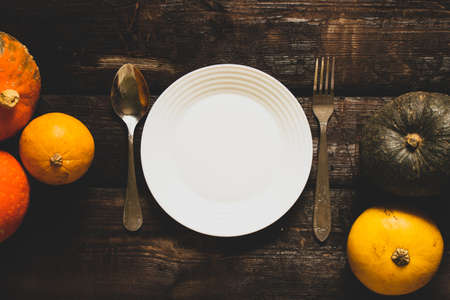 white plate on the table and next to pumpkins on an old wooden table, festive table setting decor,...