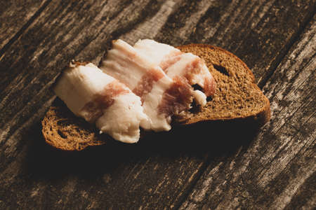 a piece of black bread and sliced bacon lies on bread on a wooden table, bread with baconの写真素材