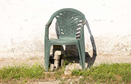 a plastic old broken chair stands on the background of a white wall of a house in summer cottages in the sun, an old chair is brokenの写真素材