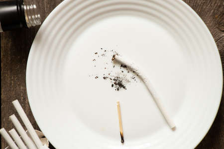 broken cigarettes on a plate on the table next to the bottle, smoking and bad habits alcoholism