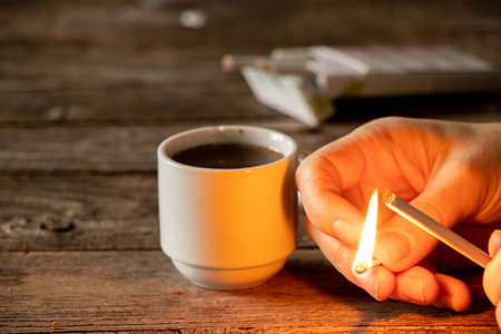 set a match on a cigarette in the hands of a girl on the table next to a cup of coffee, cigarettes and coffee, bad habitsの写真素材