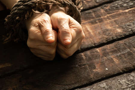 tied an old woman's hands with a rope on a wooden table, lack of will power over people, slaveの写真素材