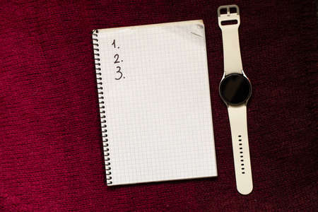 a notebook with the numbers 123 lies on a red knitted sweater and a white smart watch next to it, space for text, work planの写真素材