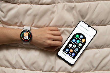 Ukraine Dnipro 11/30/2021 - Smart watch Samsung Galaxy 4.40 mm and a mobile phone with an application for Samsung on the girl's hand, technologyのeditorial素材