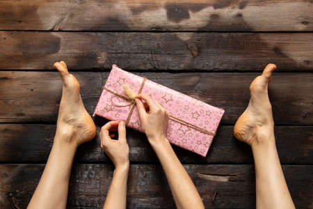 girl unfolds a birthday present on the wooden floor of the house, holiday, giving a gift