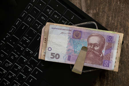 Ukrainian 50 UAH money in a money clip lie on a laptop on the table, finances and work