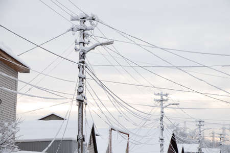 Electric wires in the snow with ice on a pole in a residential area of the city, sagging wires from the severity of snow in the city of Dnipro in Ukraineの写真素材