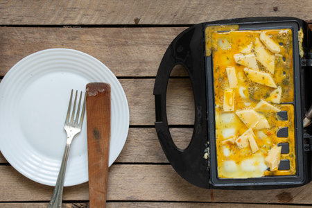 fry scrambled eggs with cheese and spices in a waffle iron on a wooden table in the kitchen, boil scrambled eggs in a waffle iron, breakfastの写真素材
