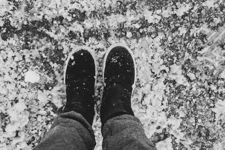 female legs in boots and gray pants on the road in wet snow in winter, feet on the road, path, winter bad weatherの写真素材