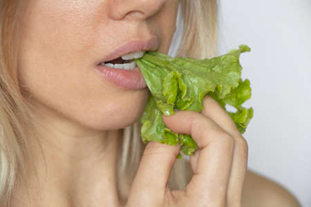 green salad in the mouth of a girl on a white background, vegetable food, on a diet, eat vegetables,...