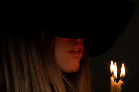 a girl in a black hat in the dark holds a candle, a girl with candles at nightの写真素材