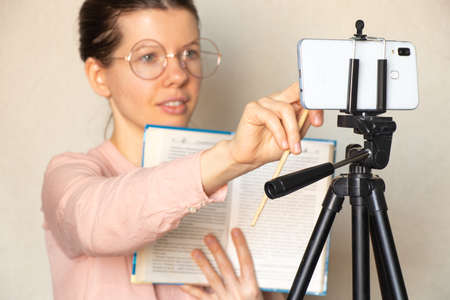 a girl conducts training with a book on the phone at home online, education online, online conference on carntinの写真素材