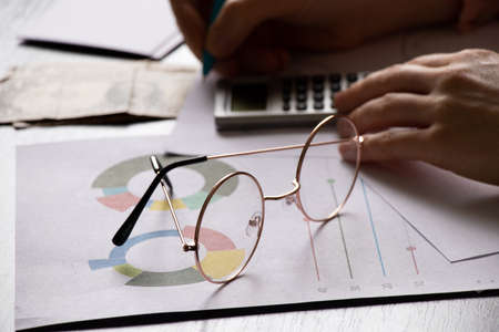 financial reports and a bar graph lie on a desk next to a calculator and glasses, business finance and economicsの写真素材