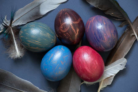 chicken decorated eggs with watercolor multi-colored paints and dove feathers on a blue background,...