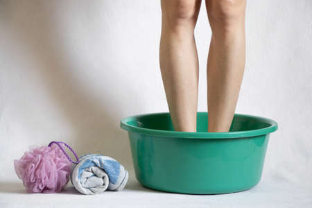a girl washes her feet in a green bowl on a white background, hygiene, beauty and relaxationの写真素材