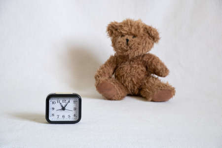 children's teddy bear and a clock on a white background, an alarm clock on the tableの写真素材