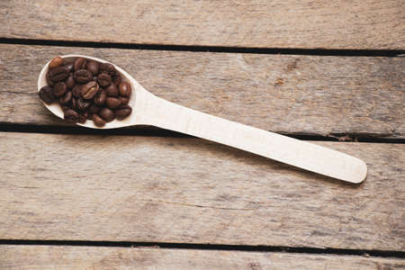 roasted coffee grains in a wooden spoon on an old wooden table in the kitchen