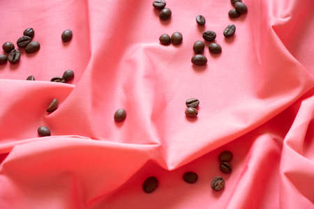 Pink wrinkled fabric and scattered grains of roasted coffee as a background, coffee for the backgroundの写真素材