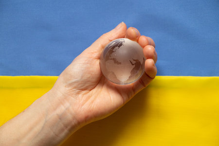 The flag of Ukraine is yellow and blue, and the hand holds the globe. Martial law in Ukraine 2022. Stop the war. Worldの写真素材