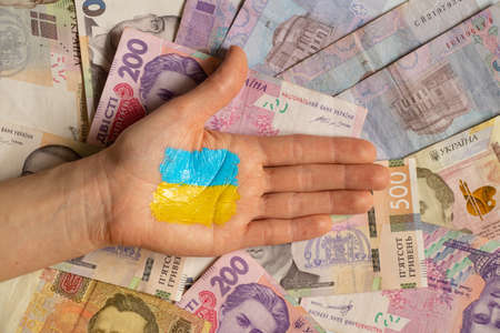 The yellow-blue flag of Ukraine is painted on the girl's hand on the background of money. Martial...