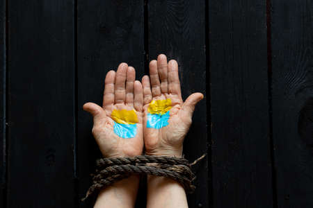 The flag of Ukraine is yellow and blue on the bound female old hands of a woman on a wooden table, Martial law in Ukraine, patriotism and Kiev, strength and powerの写真素材