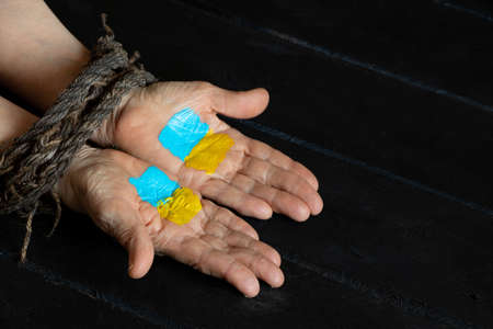 The flag of Ukraine is yellow and blue on the bound female old hands of a woman on a wooden table,...