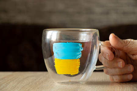 The yellow-blue national flag of Ukraine is painted on cups with coffee in the girl's hand at the...