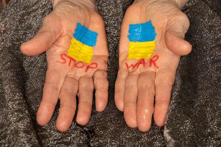 On the hands of the old woman is drawn the yellow-blue flag of Ukraine and the words stop the war, Stop the war and patriotism, peace in Ukraine, stop the war in Ukraine. Peace to all, the flag of Ukraine. Protestの写真素材