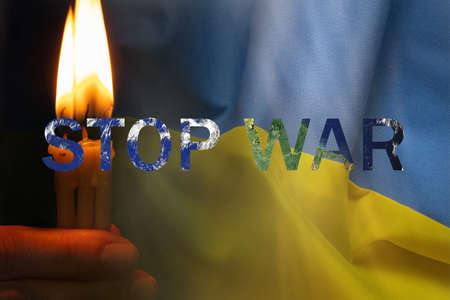 A woman's hand holds candles against the background of the flag of Ukraine and the inscription stop war. Protest action, prayer for Ukraine 2022の写真素材