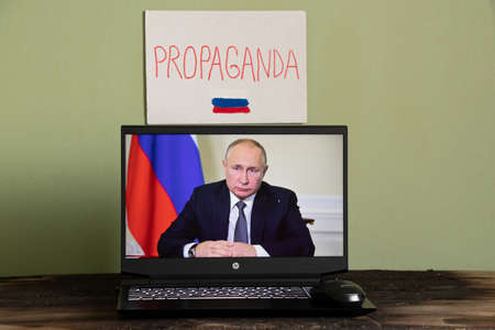 Ukraine Dnepr 06.03.2022 - Russian President Putin in the news on a laptop and a sign with the text propaganda on the wall, Putin is a killer and his propagandaのeditorial素材