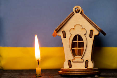 Wooden house against the background of the Flag of Ukraine and the flame of a candle, a home in Ukraine, a prayer for Ukraineの写真素材