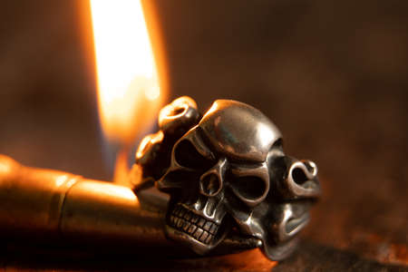 Silver ring with a skull and a bullet against the background of a candle flame in the dark, death and fear and war, weapons and gothicの写真素材