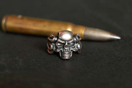 Silver ring with a skull and a bullet on a dark background, death and fear and war, weapons and gothicの写真素材