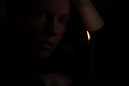 A young Ukrainian girl prays near a candle for Ukraine in Ukraine, a girl poured candles in the dark close-upの写真素材