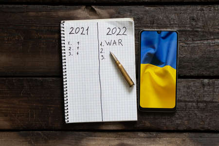 Notepad with text 2021 and 2022 Nearby lies a bullet and a phone with the flag of Ukraine, Plans for...