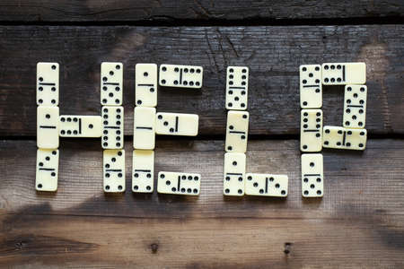 The word help is laid out from domino letters on an old wooden table close-up