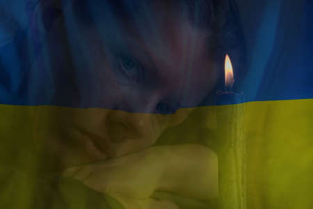 The girl lies near the candle on the background of the national flag of Ukraine, the war in Ukraine, we mourn for those who died in the war 2022の写真素材