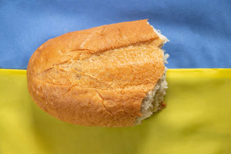 A loaf of broken bread against the background of the national flag of Ukraine yellow-blue close-upの写真素材
