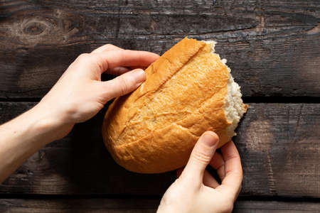 A girl holds a piece of white bread in her hands on an old wooden table, bread and harvest in...
