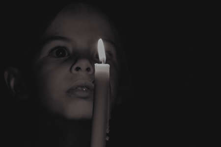 A little Ukrainian girl pray near a candle in the dark, a prayer to God for peace, religion and a candleの写真素材