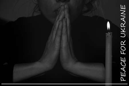 Text Peace for Ukraine. A young Ukrainian girl prays near a candle for Ukraine, black and white...