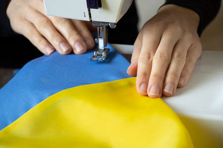 A girl sews the flag of Ukraine at home on a sewing machine, the production of national flags for...