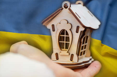 The national flag of Ukraine is yellow-blue on the background of children's hands holding a wooden small house, peace and family in Ukraine, home 2022の写真素材