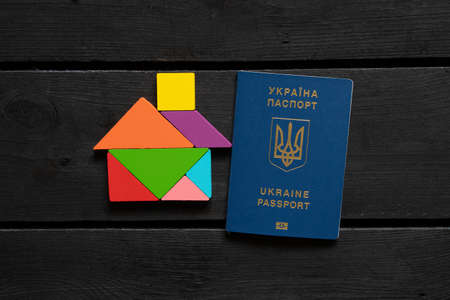 A wooden house made of cubes lies next to a Ukrainian biometric foreign passport on the table, Native Home Ukraineの写真素材